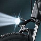 A bicycle M10 headlight shines brightly, illuminating the area ahead, with its beam cutting through the dark background. The bike's front tire and fork are visible, showcasing a sleek, modern design.
