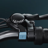A close-up of a bicycle M10 gear shifter on the handlebars, displaying numbers 1 to 7. The shifter features a prominent black dial and a blue button with a plus sign, set against a dark background.