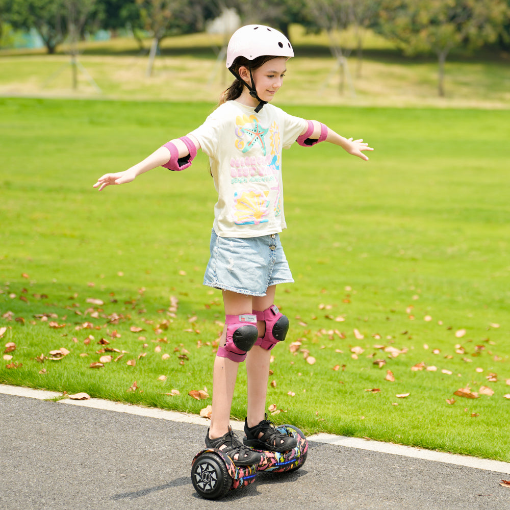 A young girl wearing a helmet and pads rides the iHoverboard Hoverboard for Kids Aged 6+ (Self Balancing, Bluetooth & LED 6.5"-H2) on a park path, surrounded by grass and trees, balancing with arms outstretched. A young girl wearing a helmet and pads rides the iHoverboard Hoverboard for Kids Aged 6+ (Self Balancing, Bluetooth & LED 6.5"-H2) on a park path, surrounded by grass and trees, balancing with arms outstretched.