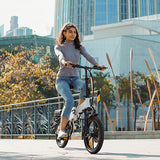 Woman riding a electric bike in an urban setting with buildings and trees in the background