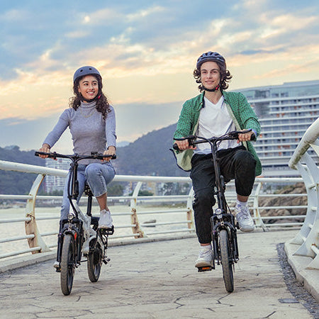 Two people riding electric bikes on a bridge with a scenic background Two people riding electric bikes on a bridge with a scenic background