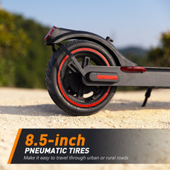 A close-up of a scooter's rear wheel with 8.5-inch pneumatic tires, featuring red accents, on a sandy path with a blurred natural background.