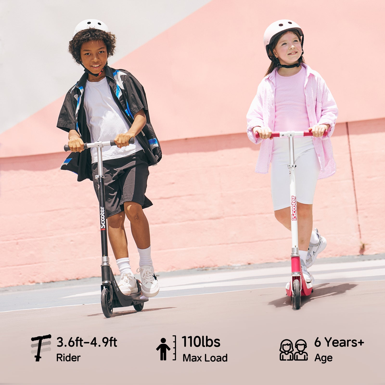Two children ride scooters ik1s on a sunny day, both wearing helmets for safety. The child on the left rides a black scooter, dressed in a black and white outfit, while the child on the right rides a pink scooter, wearing a pink jacket and white shorts. A pastel pink wall serves as the backdrop.