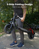 A person in casual athletic wear carries a folded black scooter GT1 with chunky tires along a paved path in a park setting, showcasing its 3-step folding design for easy portability.