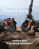 Two iSinwheel Electric Scooter 800W Foldable Off-Road E-Scooter – GT1s with large tires and orange front & rear dual shock absorbers are parked on rugged terrain. Mountains and a hazy sky frame the scene. Text: “Front & Rear Dual Shock Absorbers.”.