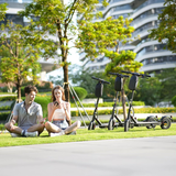 A young man and woman sit on the grass in a park, engaged with a smartphone, while three e9pro electric scooters are parked nearby. Behind them, lush trees and modern buildings create a lively urban backdrop.