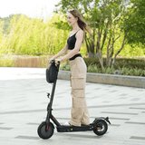 A woman rides a black e9pro electric scooter on a paved path, wearing a black crop top and beige cargo pants, with lush greenery in the background.