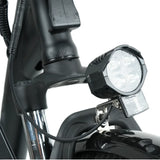 A close-up of a bicycle's front section features a bright LED headlight with four bulbs and a reflector mounted above the front wheel on a black frame.