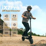 A person rides the iX7Pro Off Road EScooter on a rocky path, wearing a helmet for safety. The scooter features a powerful 2000W motor, a 50-mile max range, and 10-inch pneumatic tires, with a top speed of 38 mph and a 25% hill climbing ability.