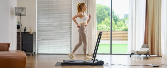 A woman in athletic wear jogs on a treadmill in a modern living room with large windows, offering a view of a green garden outside.