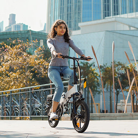 Woman riding a electric bike in an urban setting with buildings and trees in the background