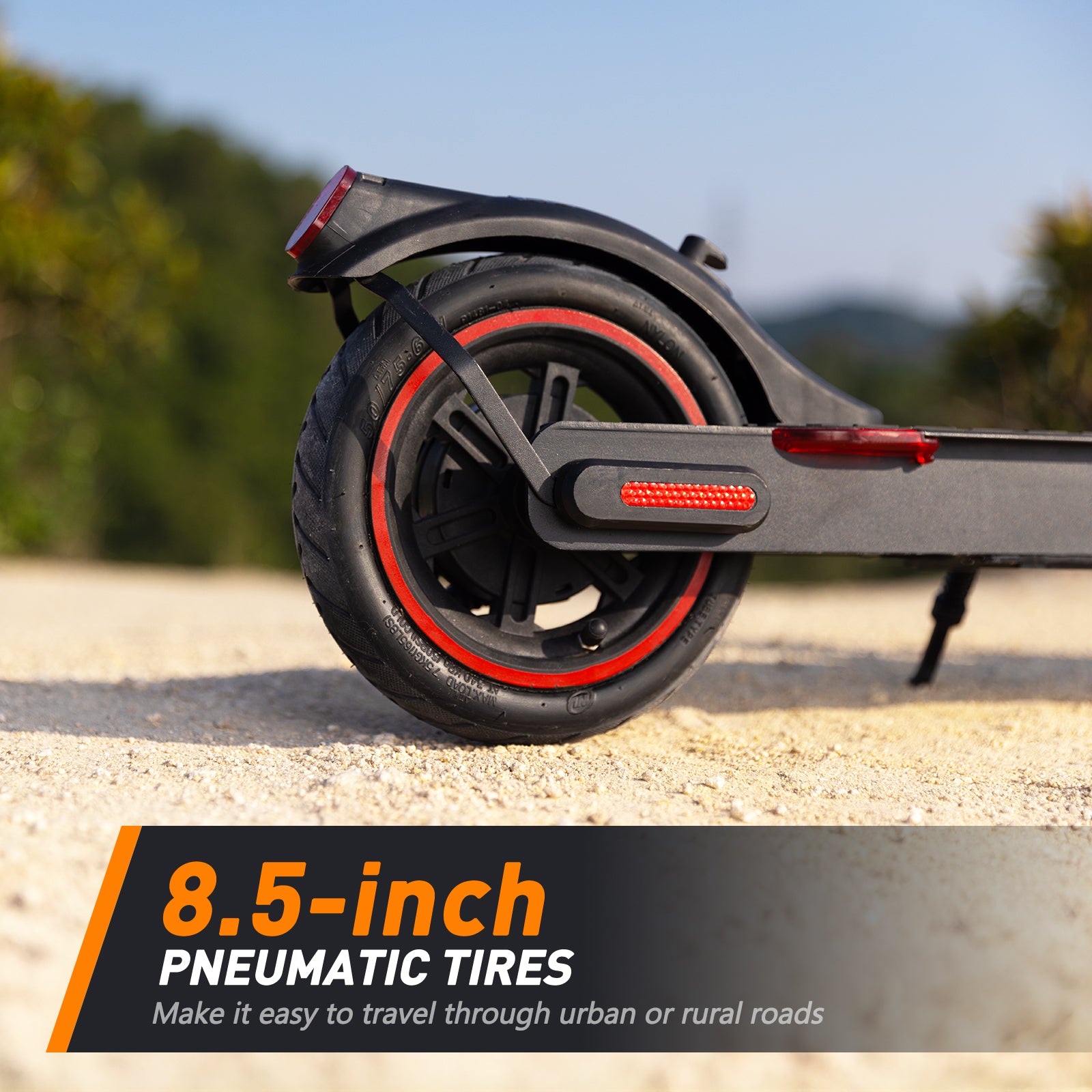 A close-up of a scooter's rear wheel with 8.5-inch pneumatic tires, featuring red accents, on a sandy path with a blurred natural background.