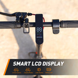 Close-up of a scooter handlebar featuring a smart LCD display showing speed and modes, with textured grips and a bell, set against a sandy background.