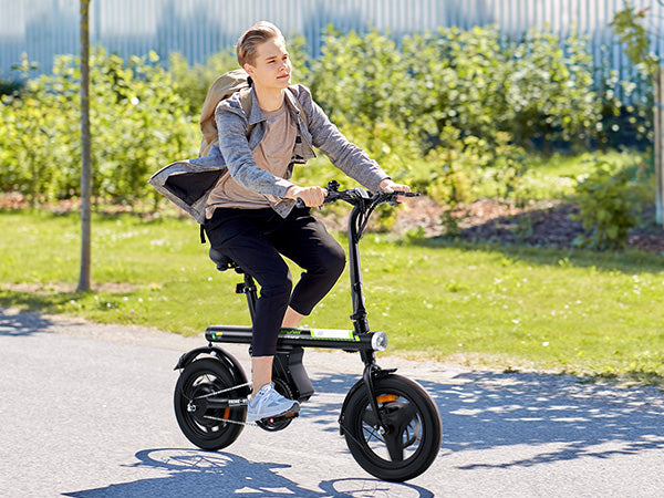 A teen riding a small electric bike on a path with greenery in the background