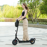Woman standing next to a black electric scooter in an outdoor setting with greenery.